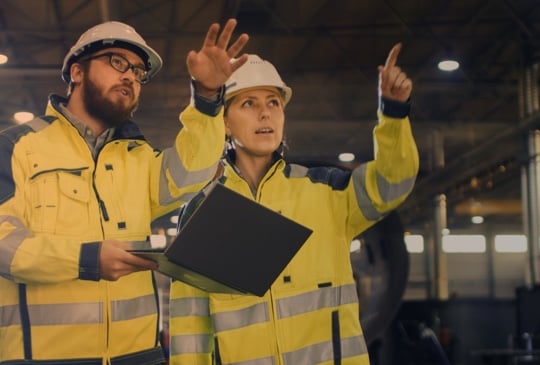 Zwei Menschen auf einer Baustelle mit Helm und gelber Jacke